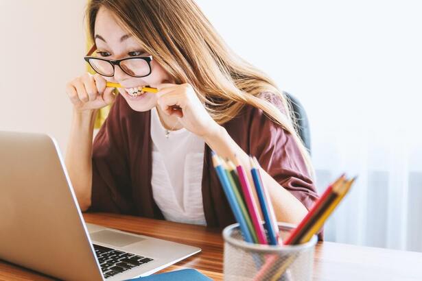 Lady with glasses sat behind a laptop chewing on a pencil in a stressful manner